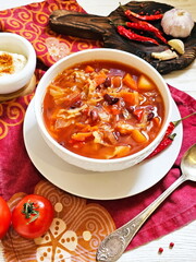 Borscht with sour cream in a white ceramic plate on a wooden background