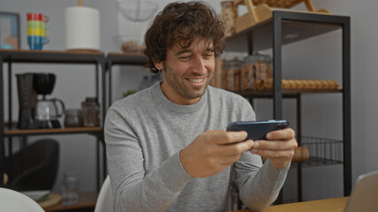 Young man in office smiling while using phone sitting at desk displaying a modern workplace atmosphere with casual style and professional setting