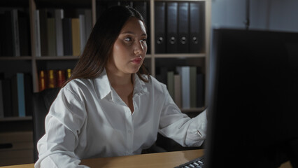Woman working on computer in indoor office with bookshelves and binders background