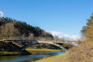 Obraz premium Early spring landscape, Concrete bridge crossing canal with blue sky in Amsterdamse Waterleidingduinen, Sand dune nature reserve with a trail in Bentveld, Dutch province of North Holland, Netherlands.