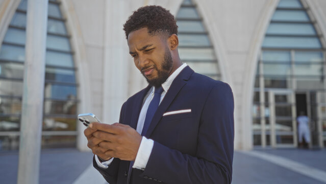 Young man dressed in a suit reading his smartphone intently on an urban street with a modern building in the background