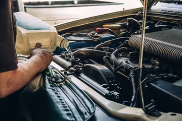 Male professional mechanic pouring antifreeze coolant liquid into car engine radiator in service center, car repair shop. Concept of car radiator coolant maintenance