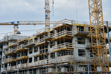 Unfinished concrete multi story building under construction with scaffolding and cranes. Modern...