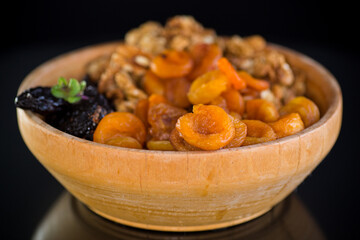 Prunes, dried apricots and nuts in a wooden bowl on a dark background