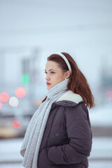 woman in warm down jacket and scarf on street in winter in city in snow