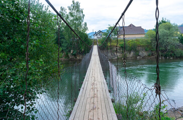 Fototapeta premium Narrow suspension wooden bridge across the Black Cheremosh River in the village of Verkhovyna. Ukraine.