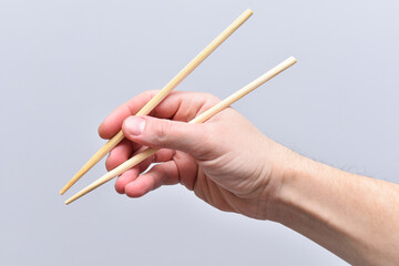 A man's hand holds wooden chopsticks for traditional oriental food
