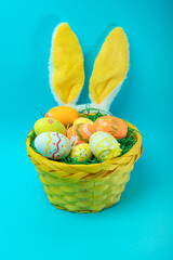 A bright yellow Easter basket filled with colorful eggs and bunny ears on a vibrant blue background. A festive holiday composition, ideal for seasonal marketing and greeting cards.