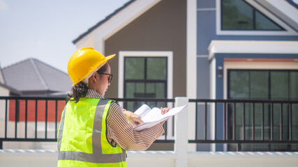 A female engineer checks the accuracy of a house blueprint in her hand at the construction site of a housing estate project.