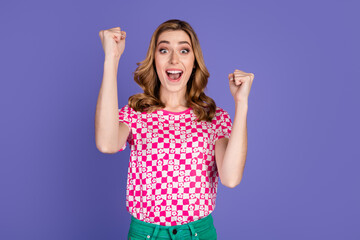 Excited young woman enjoying a celebratory moment with raised arms against a vivid violet background
