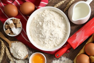 Rolling pin and ingredients for dough on wooden table, flat lay
