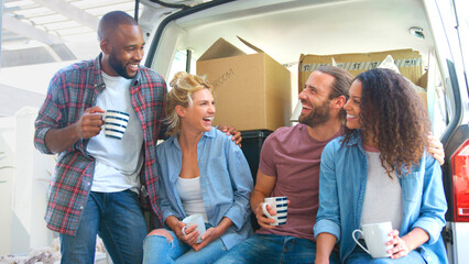 Friends Helping Couple To Unload Removal Truck On Moving Day Sitting In Back Of Truck
