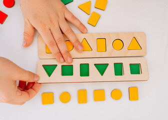 The child carefully arranges colorful wooden geometric shapes circle, square, triangle and...