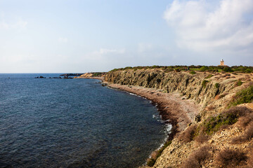 Obraz premium A scenic view of Tabarca Island, Spain, rugged coastline, clear blue waters, and a distant lighthouse under a sunny sky. Travel destination.