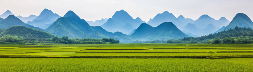 Fototapeta premium A picturesque view of lush green fields against majestic mountains under a clear sky.