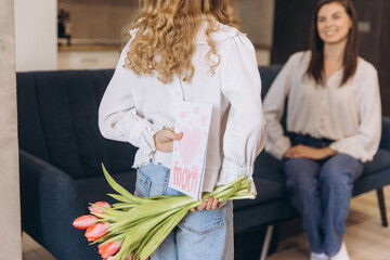 Obraz premium Daughter surprising her mother with greeting card and tulips for Mother's Day