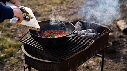 A man transfers ingredients from a cutting board into a cast iron or aluminum pot, kazan. Cooking...