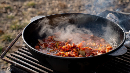 A man transfers ingredients from a cutting board into a cast iron or aluminum pot, kazan. Cooking food over an open fire.