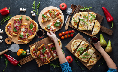 Sausage pizzas with pears, tomatoes and peppers, women's hands and a glass of wine