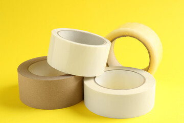 Rolls of different adhesive tapes on yellow background, closeup