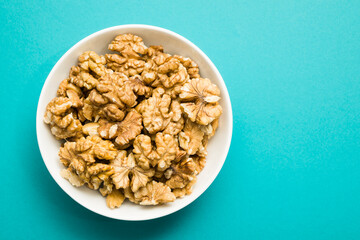 Top view of shelled walnuts into bowl on blue background.