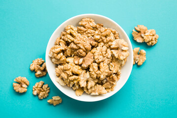 Top view of shelled walnuts into bowl on blue background.