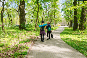 Naklejka premium Two people walking on a paved path in a lush park with blooming trees, ideal for nature, outdoor activities, and springtime themes.