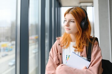 Student girl with books and a backpack listens to music in headphones