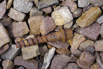 A close-up shot featuring a rusty metal bolt nestled among various rough stones, highlighting textures and contrasts.