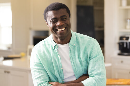 Smiling African American man in kitchen wearing casual shirt, enjoying relaxed moment at home