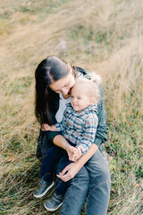 Smiling little girl sits in the arms of her mother looking at her on the lawn