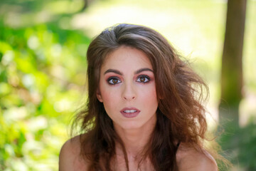 Naklejka premium A young woman with wavy hair poses in a natural setting, her expression is calm and inviting.