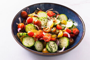 Fresh juicy summer salad with cherry tomatoes, cucumbers, aromatic dill, sweet onion and olive oil in dark ceramic bowl close up. Healthy vegan food concept.
