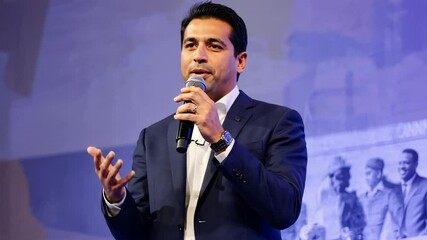 A professional Latino male speaker with microphone in hand presenting enthusiastically at a formal event. Concept of public speaking and inspirational leadership.
