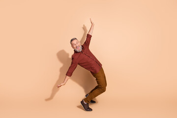 Elderly man in casual attire striking a playful pose against a beige background expressing enjoyment and positive energy