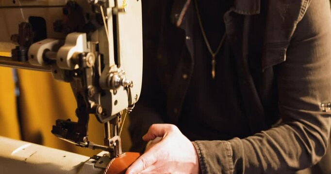 Close-up of artisan's hands meticulously stitching brown leather belt using vintage sewing machine, showcasing craftsmanship and traditional leatherwork