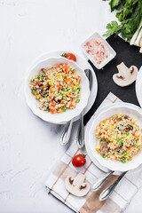 Couscous is a dish made from wheat grains (semolina) or millet. Lean couscous with mushrooms, corn, peas, herbs, tomatoes. Top view. Flatlay. Couscous on a light background.