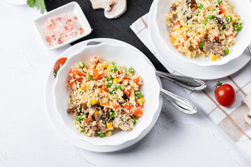 Couscous is a dish made from wheat grains (semolina) or millet. Lean couscous with mushrooms, corn, peas, herbs, tomatoes. Side view. Flatlay. Couscous on a light background. Couscous in a white plate