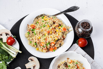 Couscous is a dish made from wheat grains (semolina) or millet. Lean couscous with mushrooms, corn, peas, herbs, tomatoes. Side view. Flatlay. Couscous on a light background. Couscous in a white plate