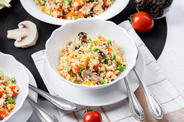 Couscous is a dish made from wheat grains (semolina) or millet. Lean couscous with mushrooms, corn, peas, herbs, tomatoes. Side view. Flatlay. Couscous on a light background. Couscous in a white plate
