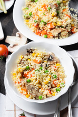 Couscous is a dish made from wheat grains (semolina) or millet. Lean couscous with mushrooms, corn, peas, herbs, tomatoes. Side view. Flatlay. Couscous on a light background. Couscous in a white plate