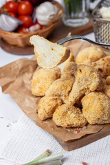 Cauliflower fries cut into slices on a fork, lean dish, cauliflower in batter. Healthy fast food. Low-calorie food fries. Cabbage, tomatoes. Deep fryer. High quality photo.