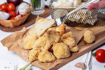 Cauliflower fries cut into slices on a fork, lean dish, cauliflower in batter. Healthy fast food. Low-calorie food fries. Cabbage, tomatoes. Deep fryer. High quality photo.