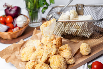 Cauliflower fries cut into slices on a fork, lean dish, cauliflower in batter. Healthy fast food. Low-calorie food fries. Cabbage, tomatoes. Deep fryer. High quality photo.
