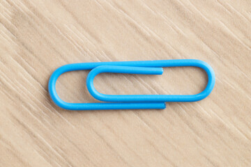 One blue paper clip on wooden table, top view