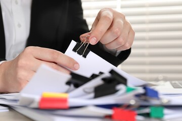 Woman attaching sheets of paper with metal binder clip at table, closeup