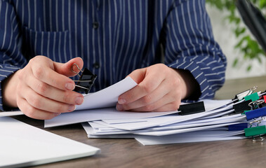 Woman attaching sheets of paper with metal binder clip at table, closeup