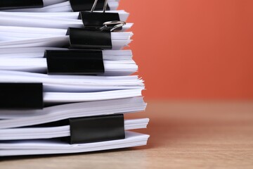 Binder clips with sheets of paper on wooden table against orange background, closeup. Space for text