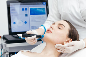 Fototapeta premium A professional performs a hydropeeling facial treatment on a young woman in a modern salon, cleansing and revitalizing the skin. Concept of using innovative technologies for skin improvement.