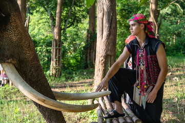Young male local Akha hilltribe mahout in traditional clothing standing with friendly Asian...